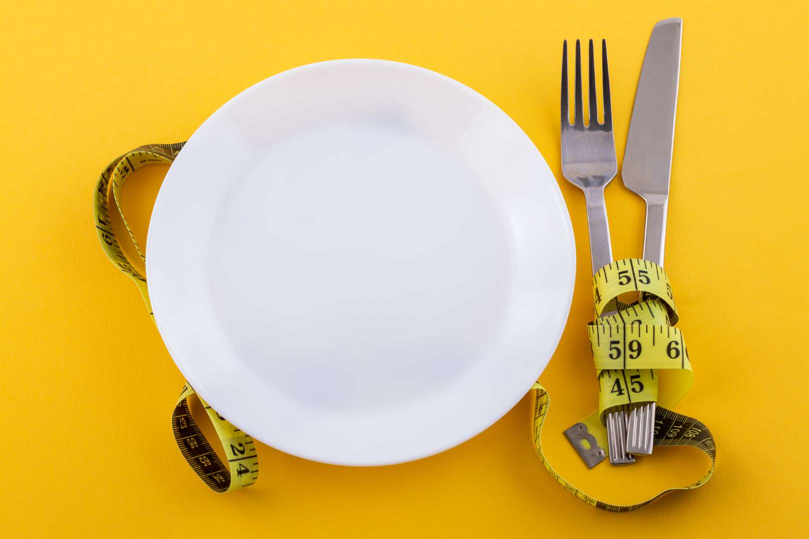 Cutlery and a white plate with measuring tape on a yellow background