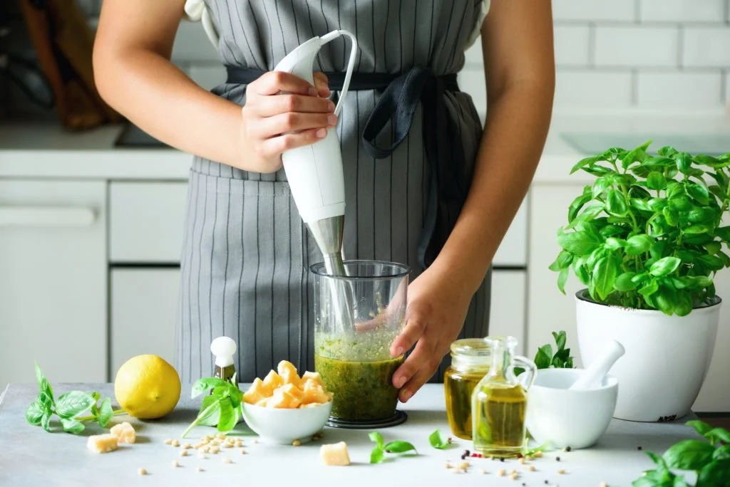 WomanIshrana posle ugradnje stenta u jednjak using hand blender to make pesto. White kitchen interior design. Copy space. Vegetarian, clean